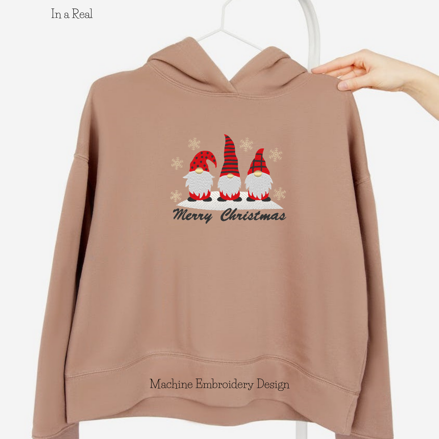 A machine embroidery design featuring Christmas gnomes, 'Merry Christmas' lettering, and delicate snowflakes is displayed on a hoodie 